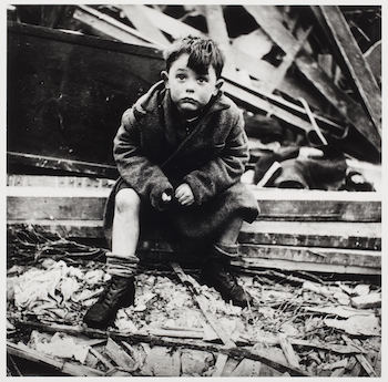 Boy sitting in the rubble of his home where his parents lie buried after a V2 bomb hit, London. Toni Frissell